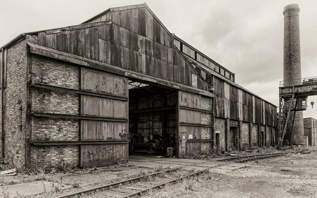 Abandoned industrial warehouse with railway tracks, showcasing historic factory architecture.